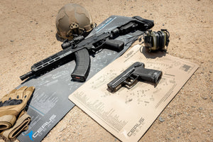 Tactical rifles and handguns placed on Cerus Gear gun cleaning mats in an outdoor range setting.
