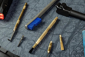 Gun cleaning tools including brass brushes, picks, and scrapers laid out on a topographic-pattern Cerus Gear mat.