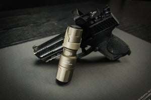 A tactical handgun with a flashlight attached, placed on a dark gray surface.
