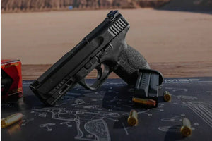 Black handgun with magazine and bullets on a Cerus Gear gun cleaning mat with printed firearm diagram outdoors.