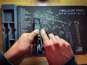 A person assembling or disassembling a Hellcat Pro Springfield handgun on a Cerus Gear mat showing part names.
