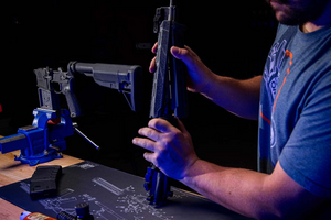 Man assembling an AR-15 rifle upper receiver using a Cerus Gear gun cleaning mat and tools.