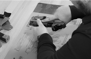 A person performing maintenance on a handgun over a Cerus Gear cleaning mat featuring labeled firearm diagrams and instructions.